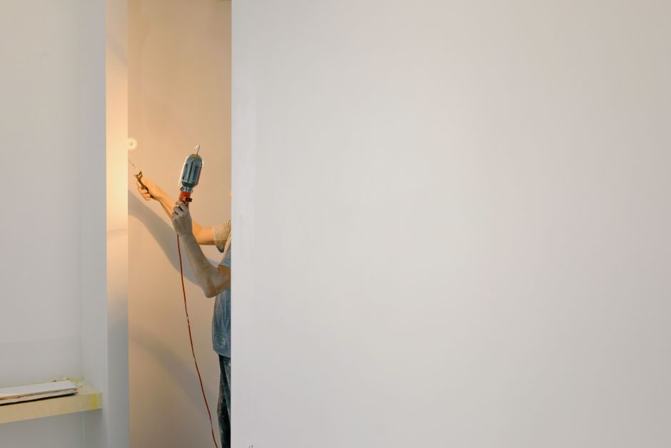 Person holding a work lamp and paint roller beside a wall
