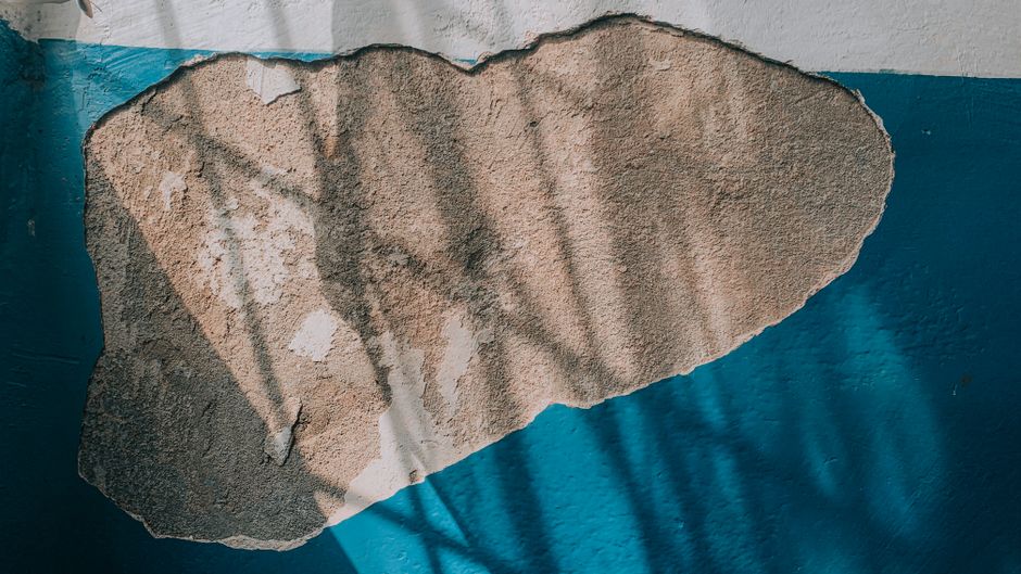 Wall with peeling blue paint and exposed plaster.