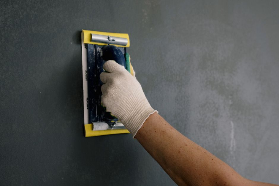 Person in white gloves holding a scraper against a wall